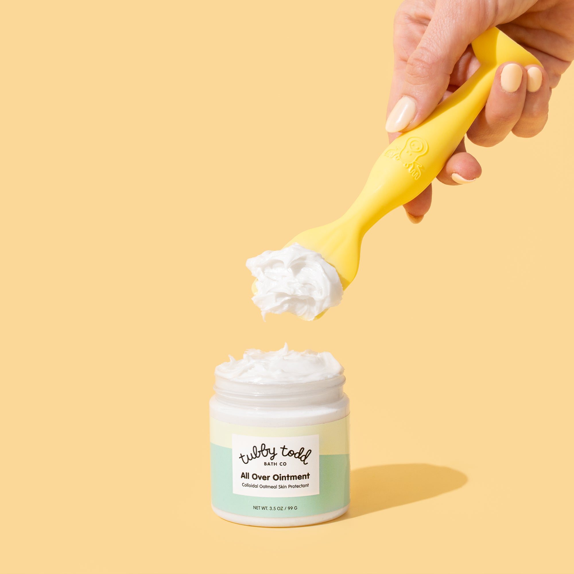 Holding a silicone spatula in hand, scooping out All Over Ointment.